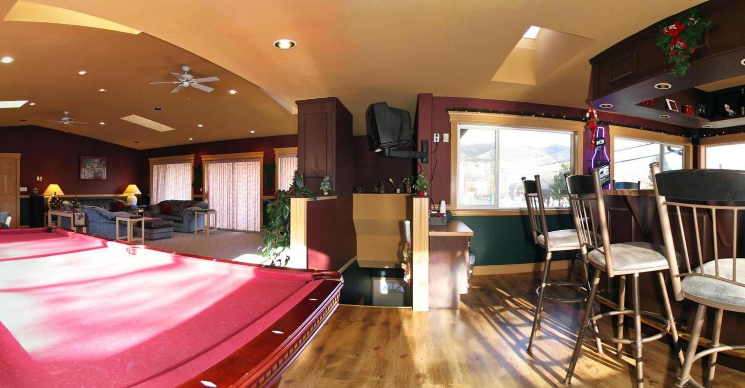 A spacious living area with a pool table, a bar area with stools, and a seating area with a couch and chairs.