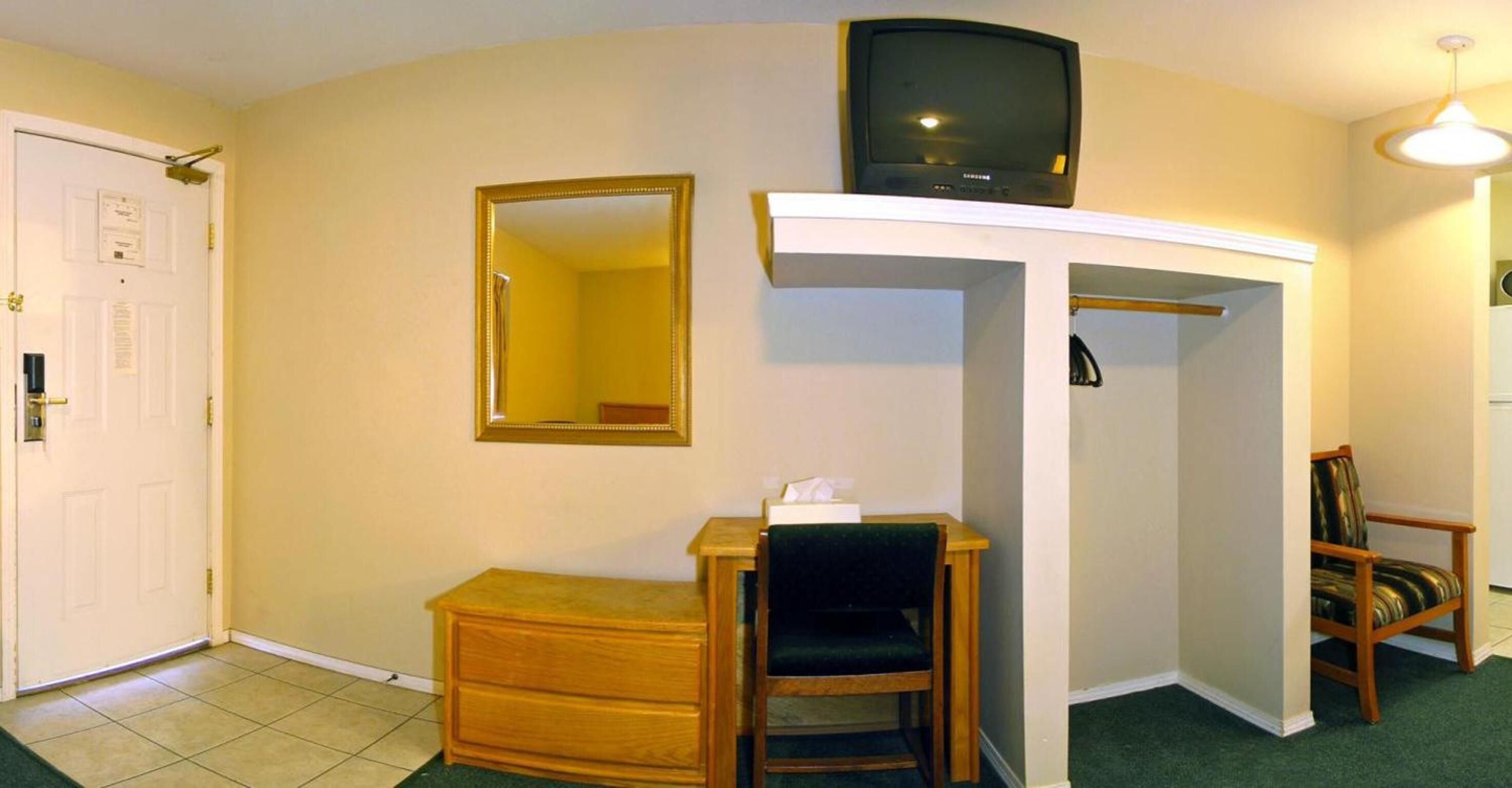 Una habitación pequeña con un aparador de madera, un espejo, un televisor sobre un mueble bajo y una silla.