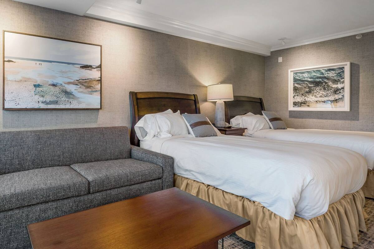 A hotel room with two beds, a sofa, a wooden table, and artwork on the walls.