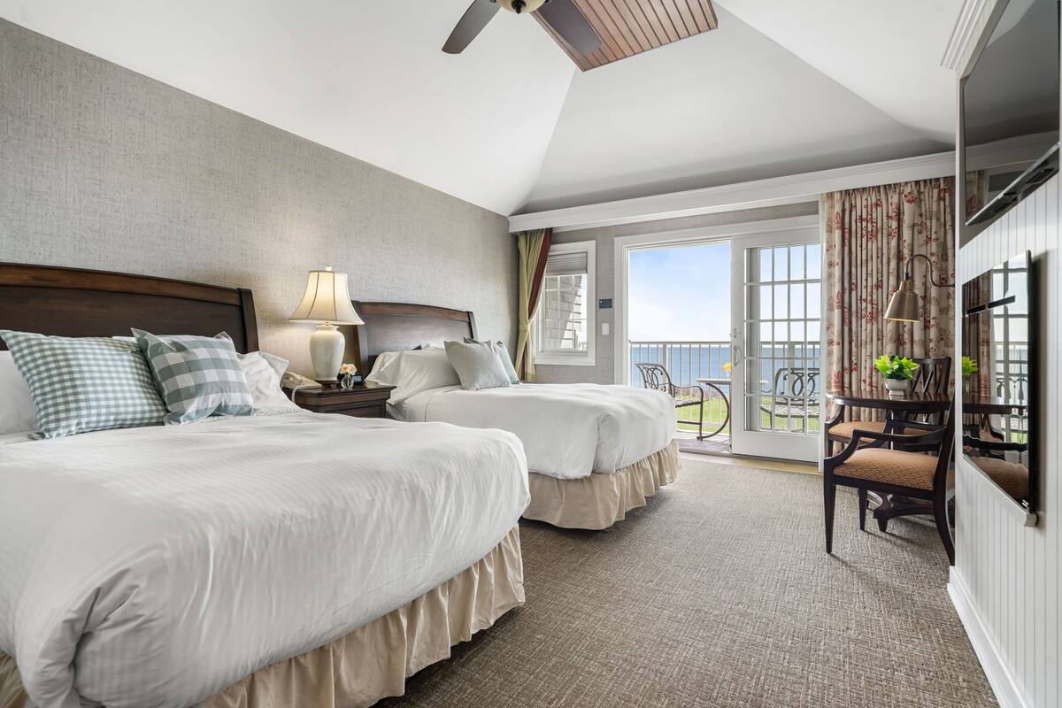 A hotel room with two beds, a balcony with a view, a ceiling fan, and a TV.