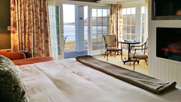 Habitación de hotel con cama, una silla, una mesa y vista al agua a través de la puerta.
