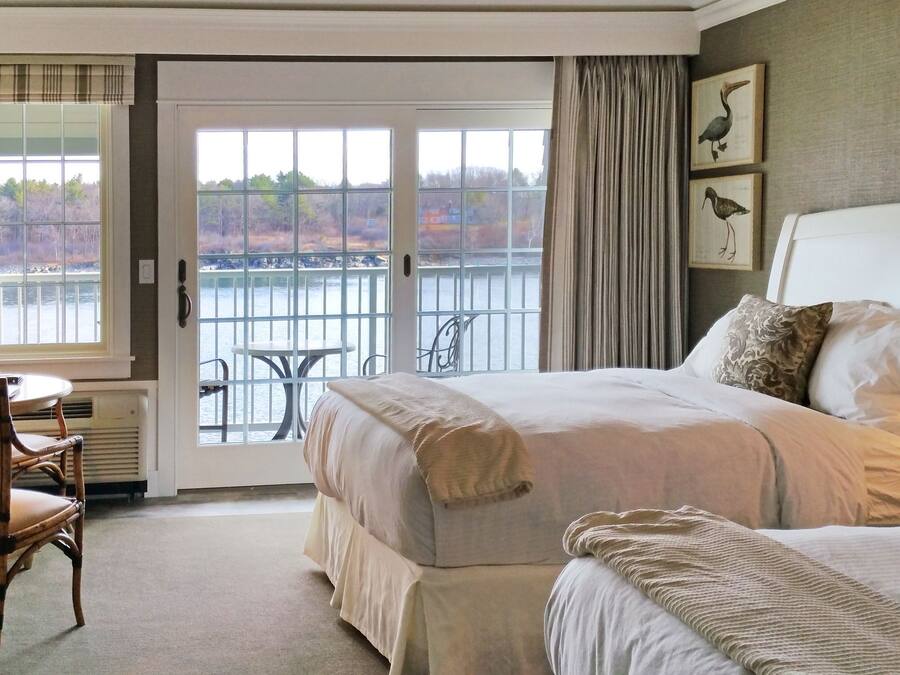 A hotel room with a bed, a desk with a lamp, a chair, and a view of a body of water through a glass door.