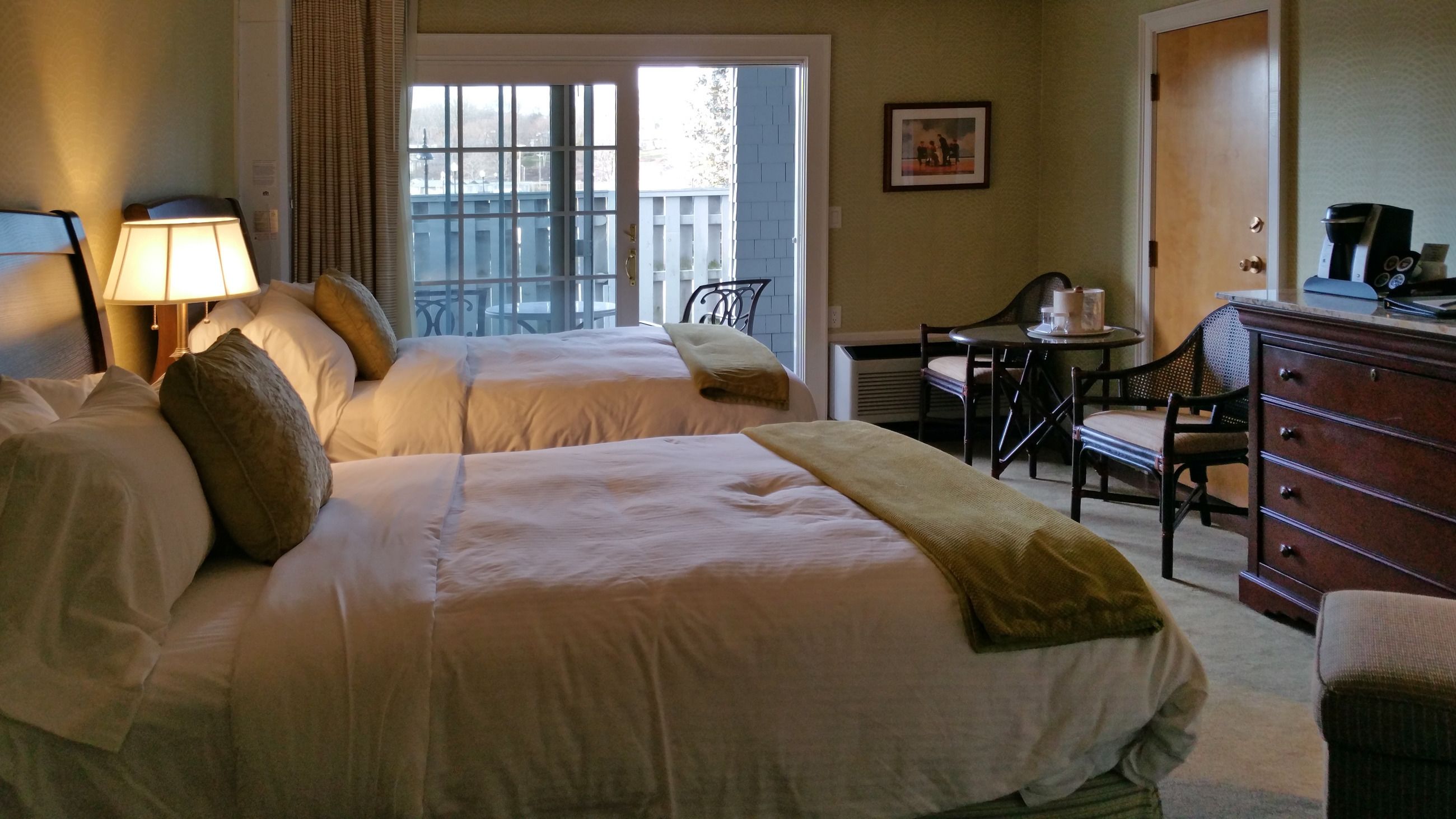 Habitación de hotel con dos camas, un escritorio, una silla, un aparador y una ventana con vista a un balcón.