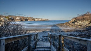 Una escalera de madera que conduce a una playa, con vistas claras al océano y casas al fondo.