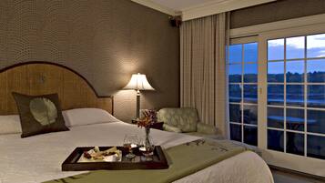Une chambre d’hôtel avec un grand lit, une table de chevet avec une lampe, un plateau avec de la nourriture et des boissons, et une vue sur l’extérieur par une fenêtre.