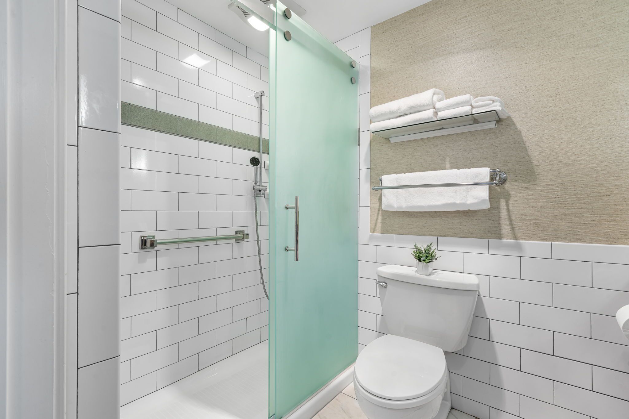 Ein modernes Badezimmer mit weißen Fliesen, einer Duschkabine aus Glas, einer weißen Toilette und einem Handtuchhalter.