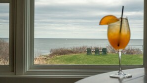 Vista del océano a través de una ventana, con un vaso de jugo de naranja sobre una mesa.