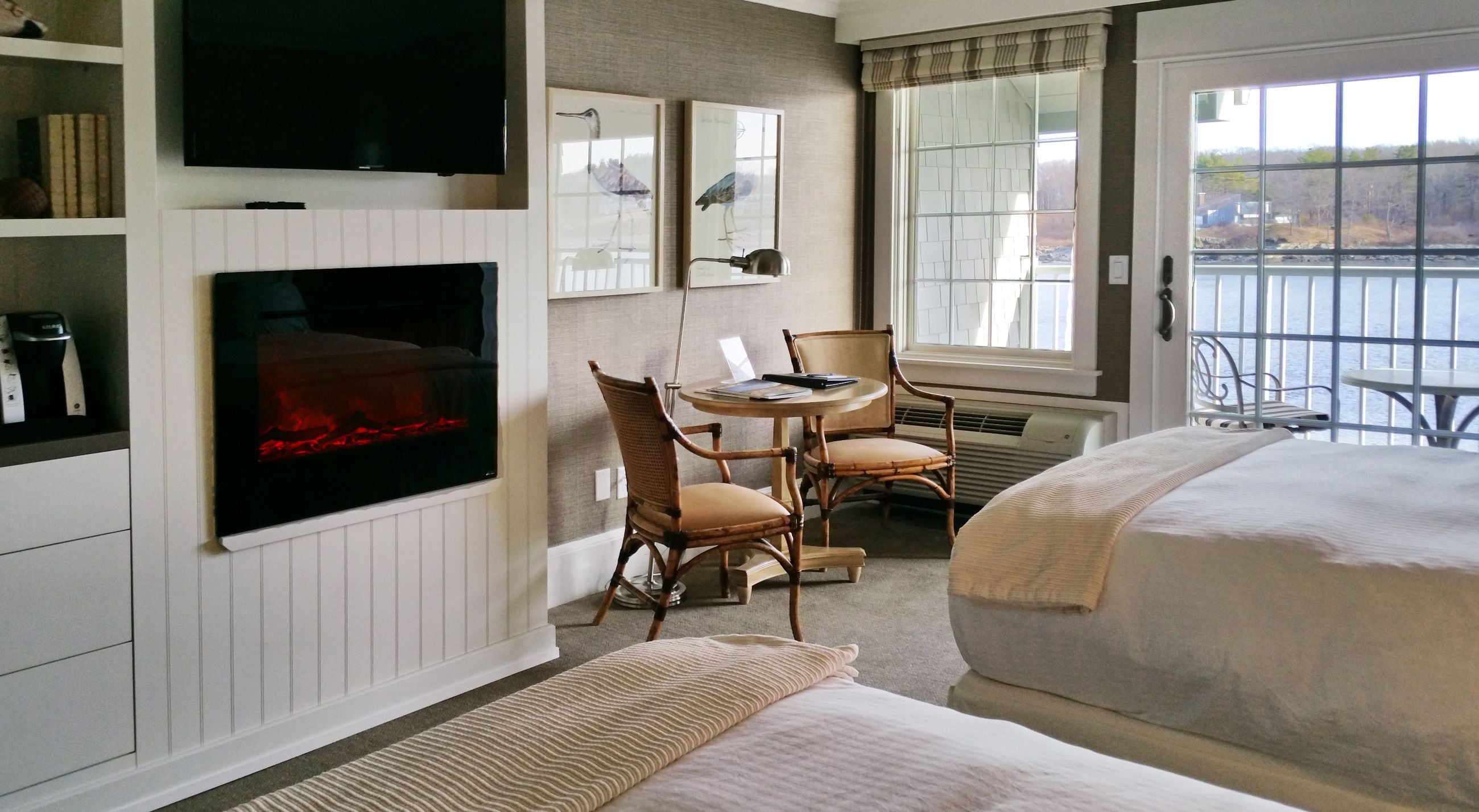 A hotel room with a bed, a desk with chairs, a TV, and a window with a view of a body of water.