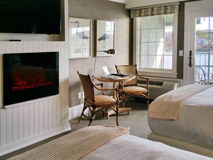 A hotel room with a bed, a desk with chairs, a TV, and a window with a view of a body of water.