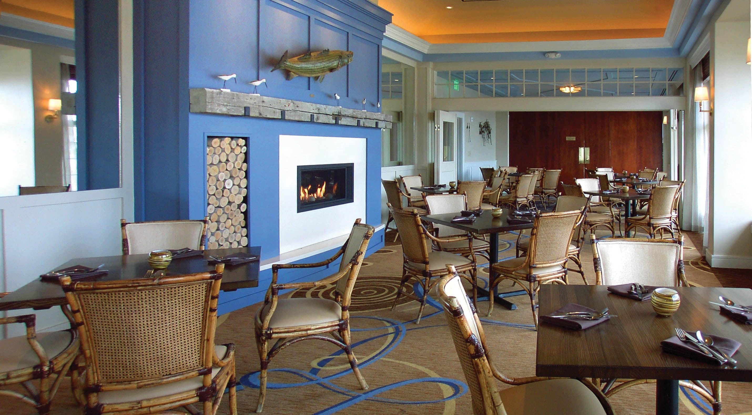 Comedor de hotel con sillas de mimbre, una chimenea y vistas al pasillo.