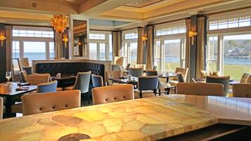 Een restaurant met een tafel van natuursteen, zachte zittingen en grote ramen met uitzicht op zee.