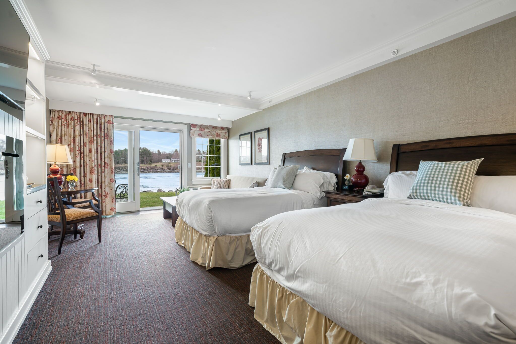 A hotel room with two beds, a dining area, and a view of the outdoors.