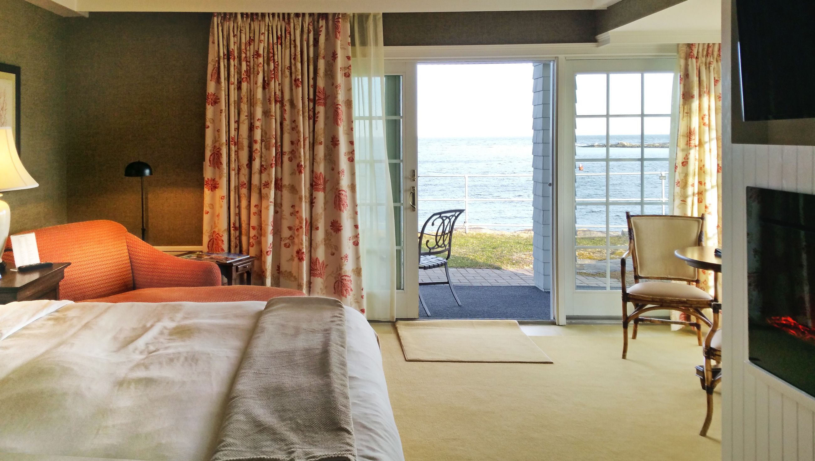 A hotel room with a bed, a chair, a table, and a view of the sea through an open door.
