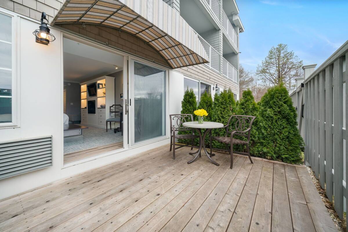 A wooden deck with a table and chairs, a covered patio area, and a view of the interior of a house.