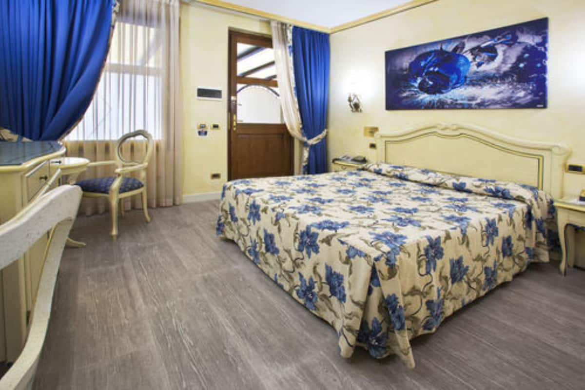 A hotel room with a bed, a desk, a chair, and a painting on the wall.