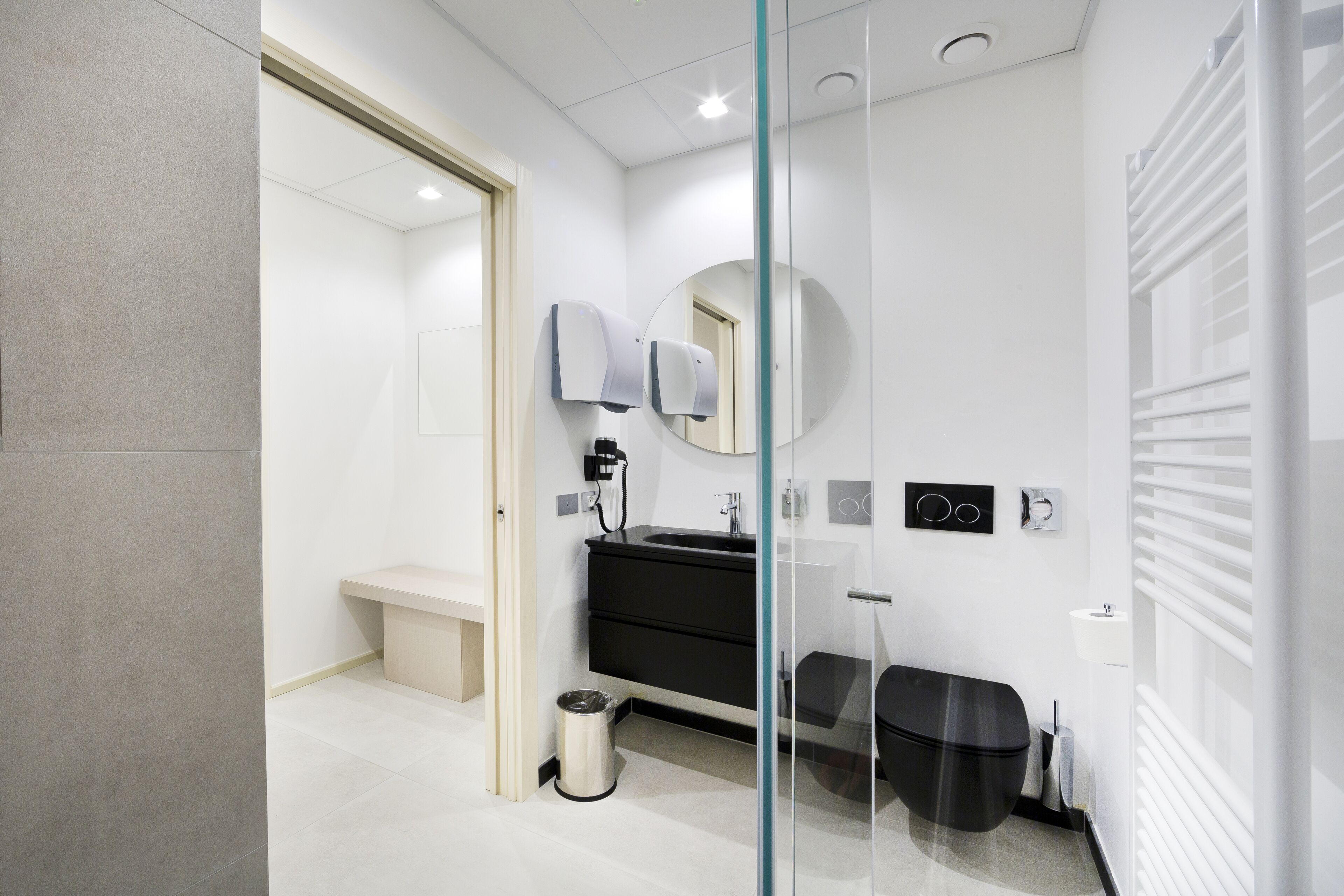 A modern bathroom with a glass partition, a black vanity, a round mirror, and a toilet.