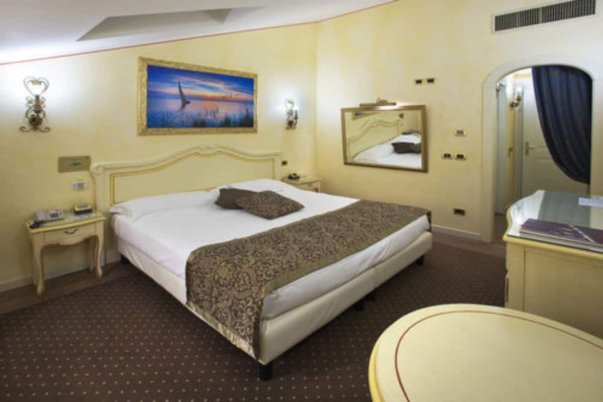 A hotel room with a large bed, a bedside table with a lamp, a mirror, and a dresser.