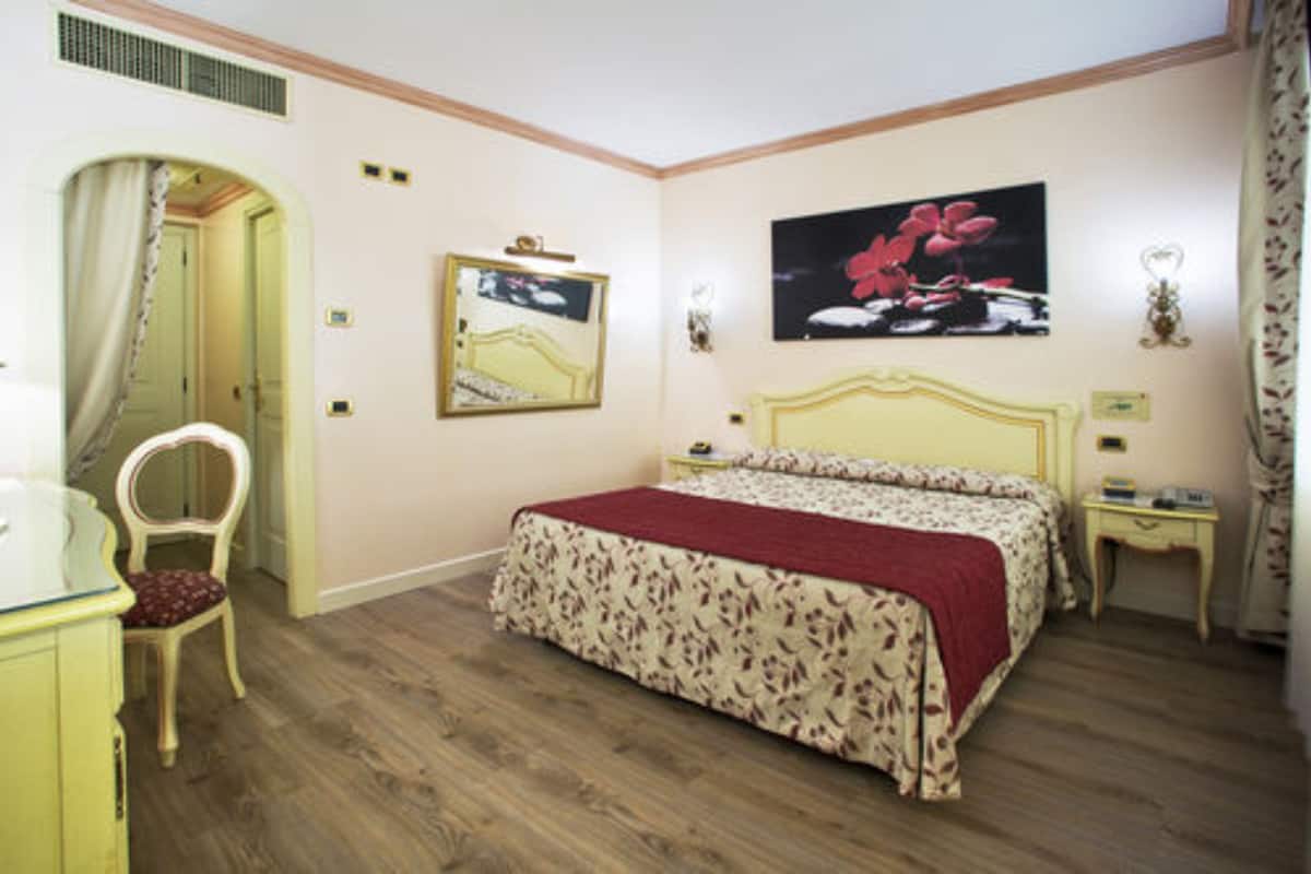 A bedroom with a bed, a chair, a nightstand, and a wall-mounted lamp.
