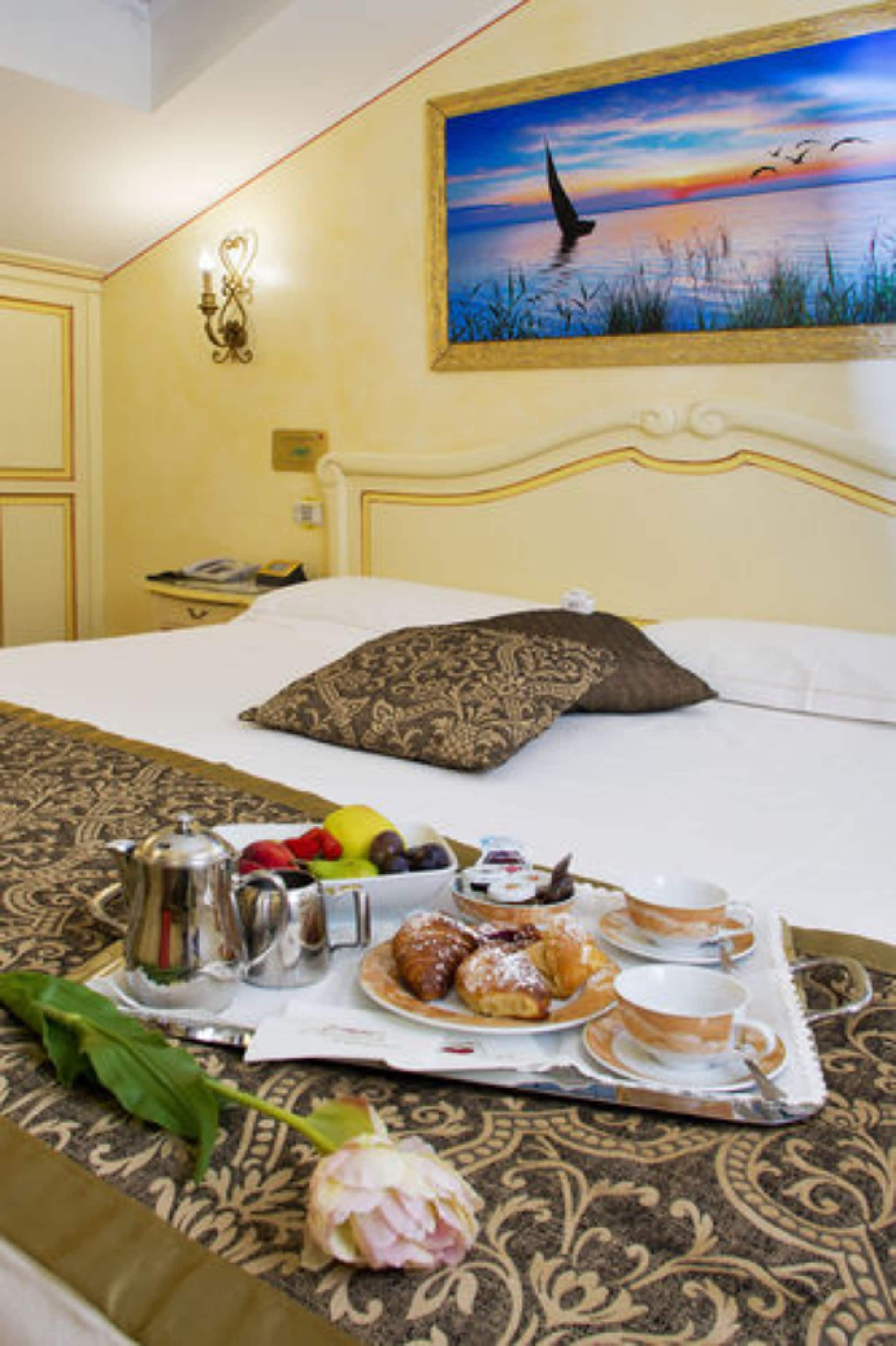 A hotel room with a bed, a painting of a bird in flight, a tray with breakfast items, and a telephone on the nightstand.