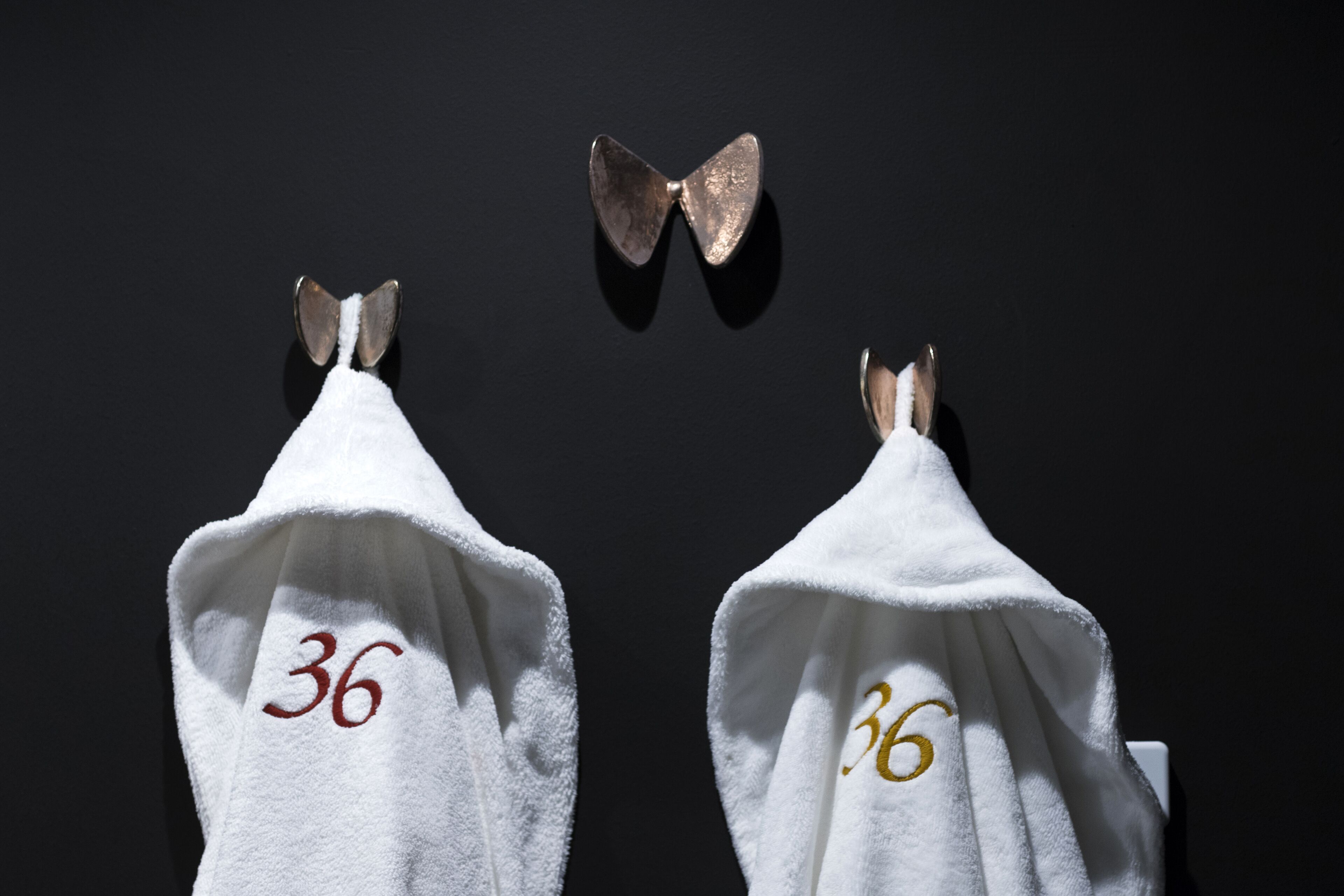 Deux serviettes blanches, portant le numéro 36, sont accrochées à un mur sombre.