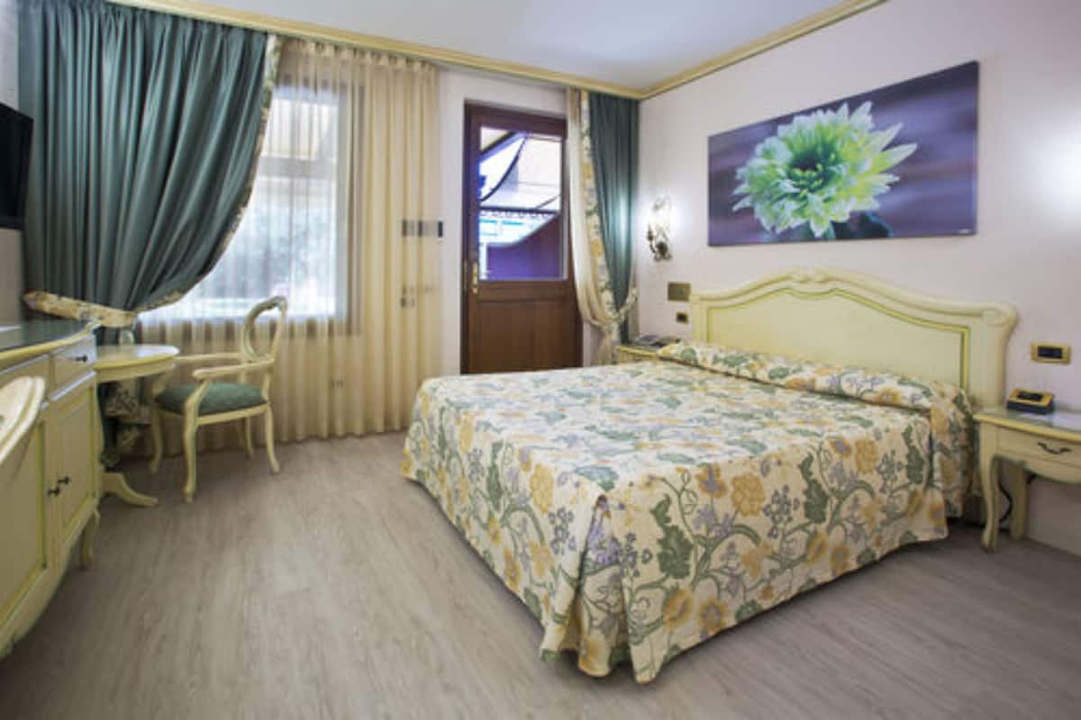 A hotel room with a bed, a desk, a chair, and a painting.