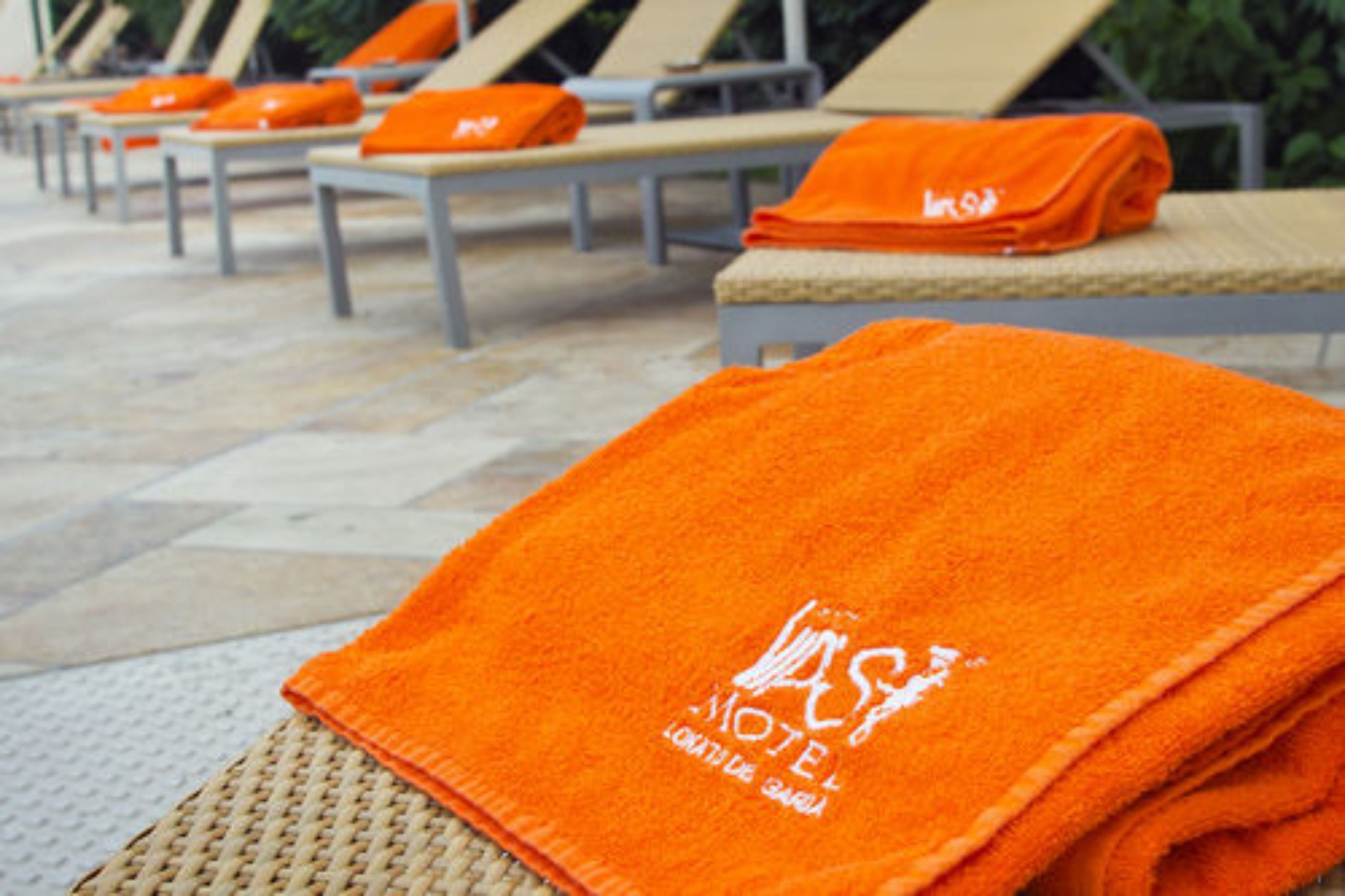 A row of lounge chairs with orange towels folded on them, indicating a hotel or resort setting.