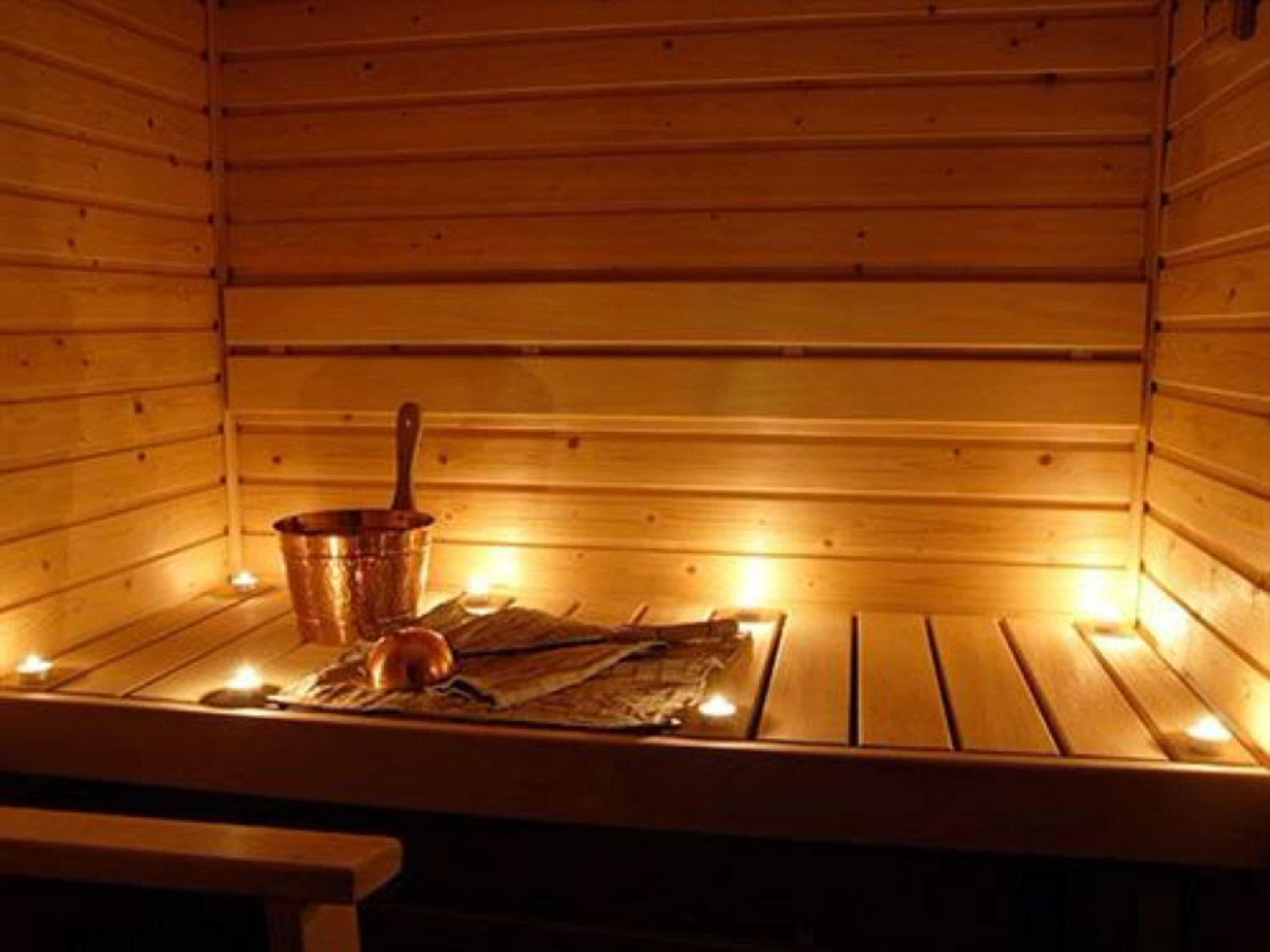Een sauna met houten wanden, een koperen emmer en kaarsen.