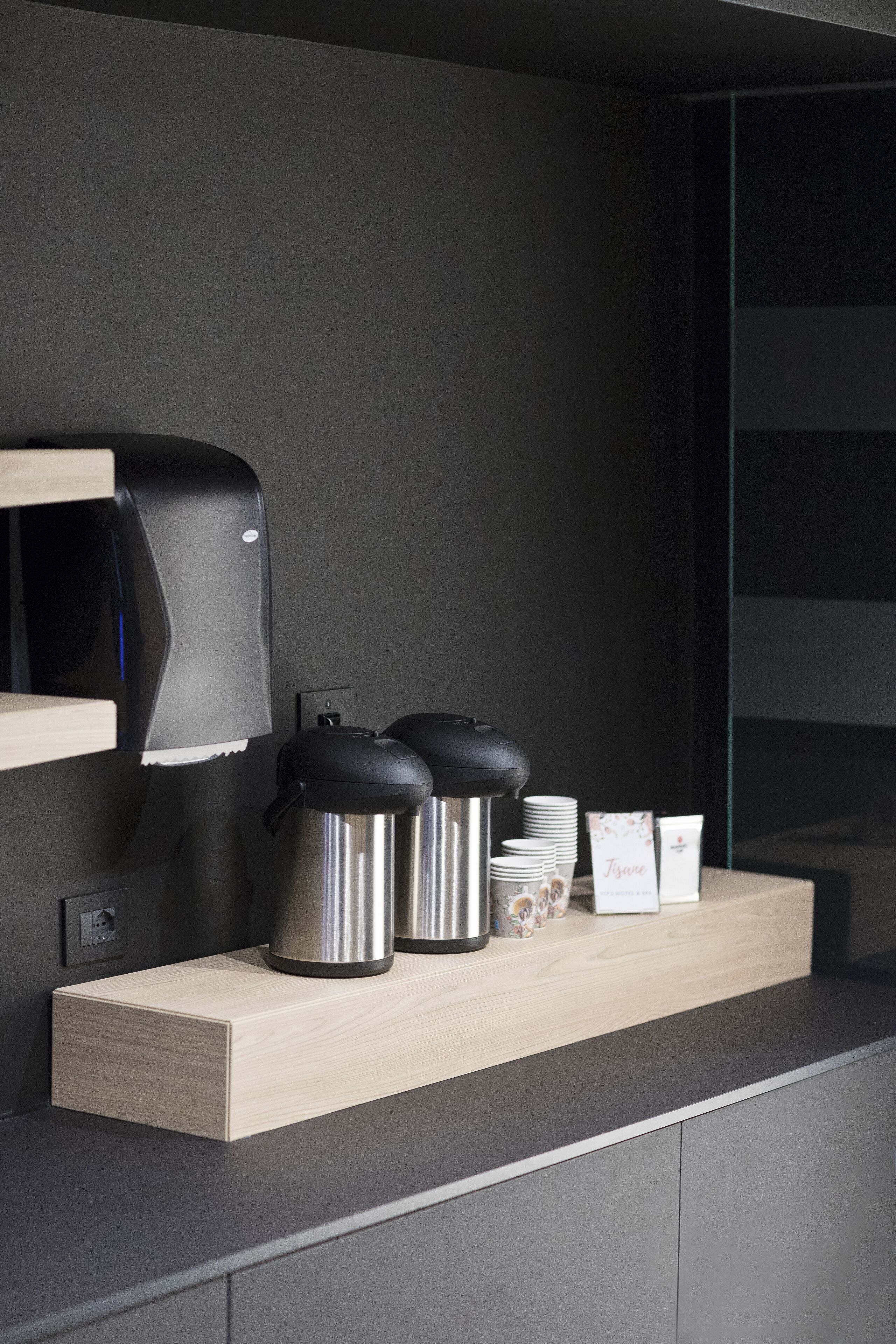 A modern kitchen area with a coffee machine, stainless steel containers, and a wooden counter.
