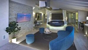 Una moderna camera d'albergo con una grande TV, un'area salotto confortevole, un tavolino e vista mare.