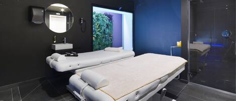 Un moderno spa con dos camillas de masaje, un espejo montado en la pared y una zona de ducha con paredes de vidrio.
