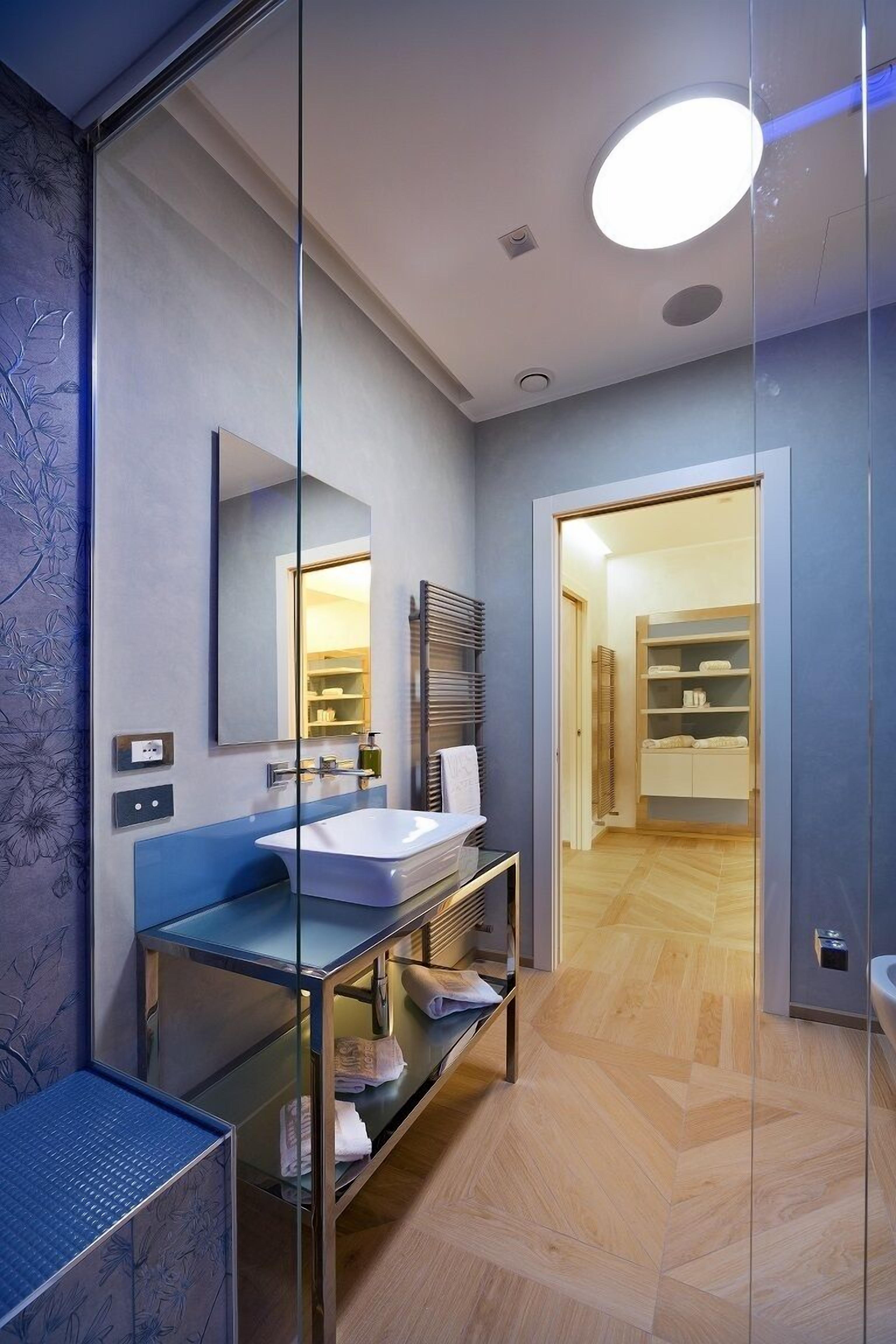 A modern bathroom with a glass partition, a sink, a mirror, and a walk-in closet with shelves.