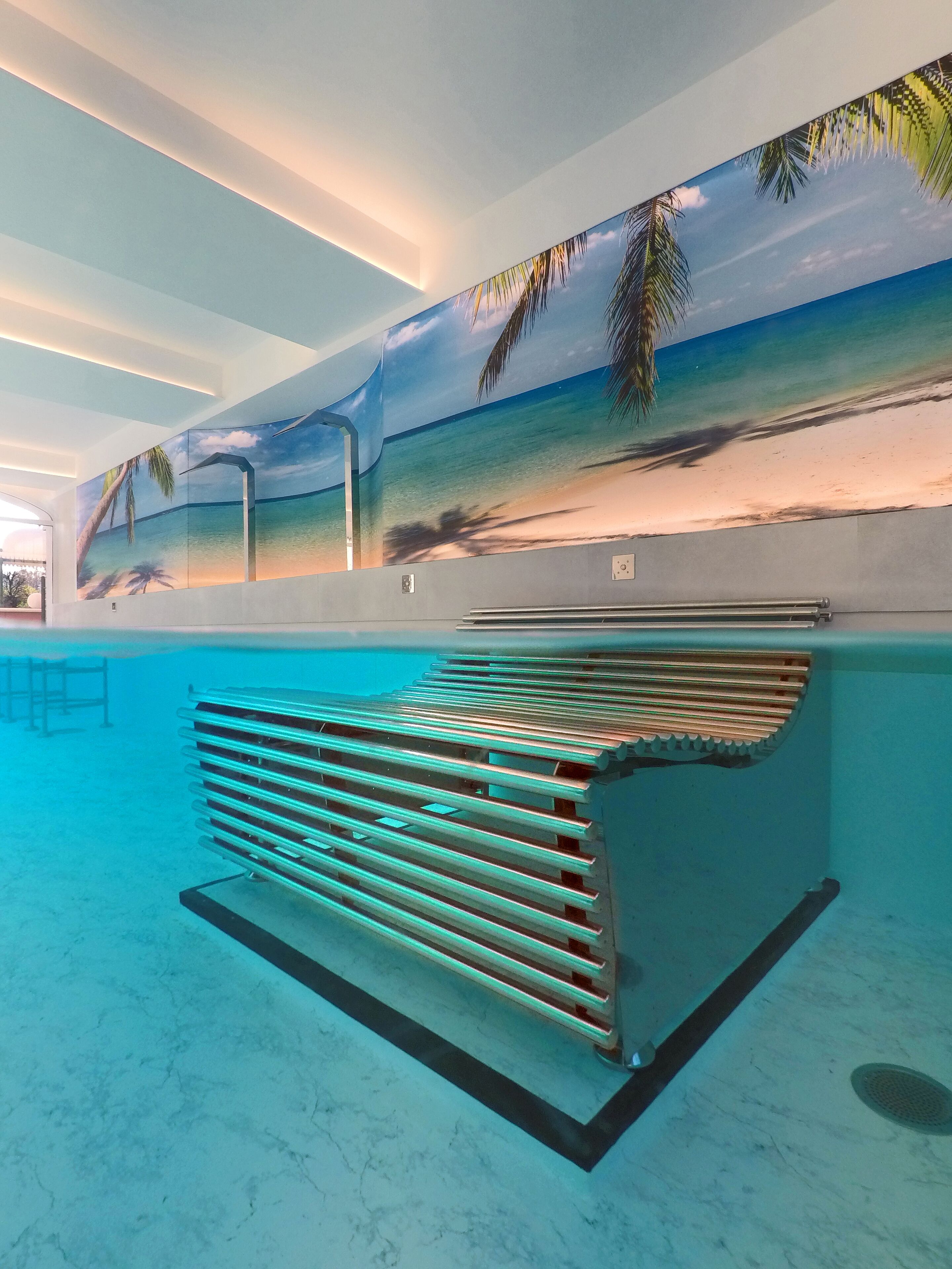 Une piscine dont le mur du fond est décoré d’une fresque représentant une scène de plage.