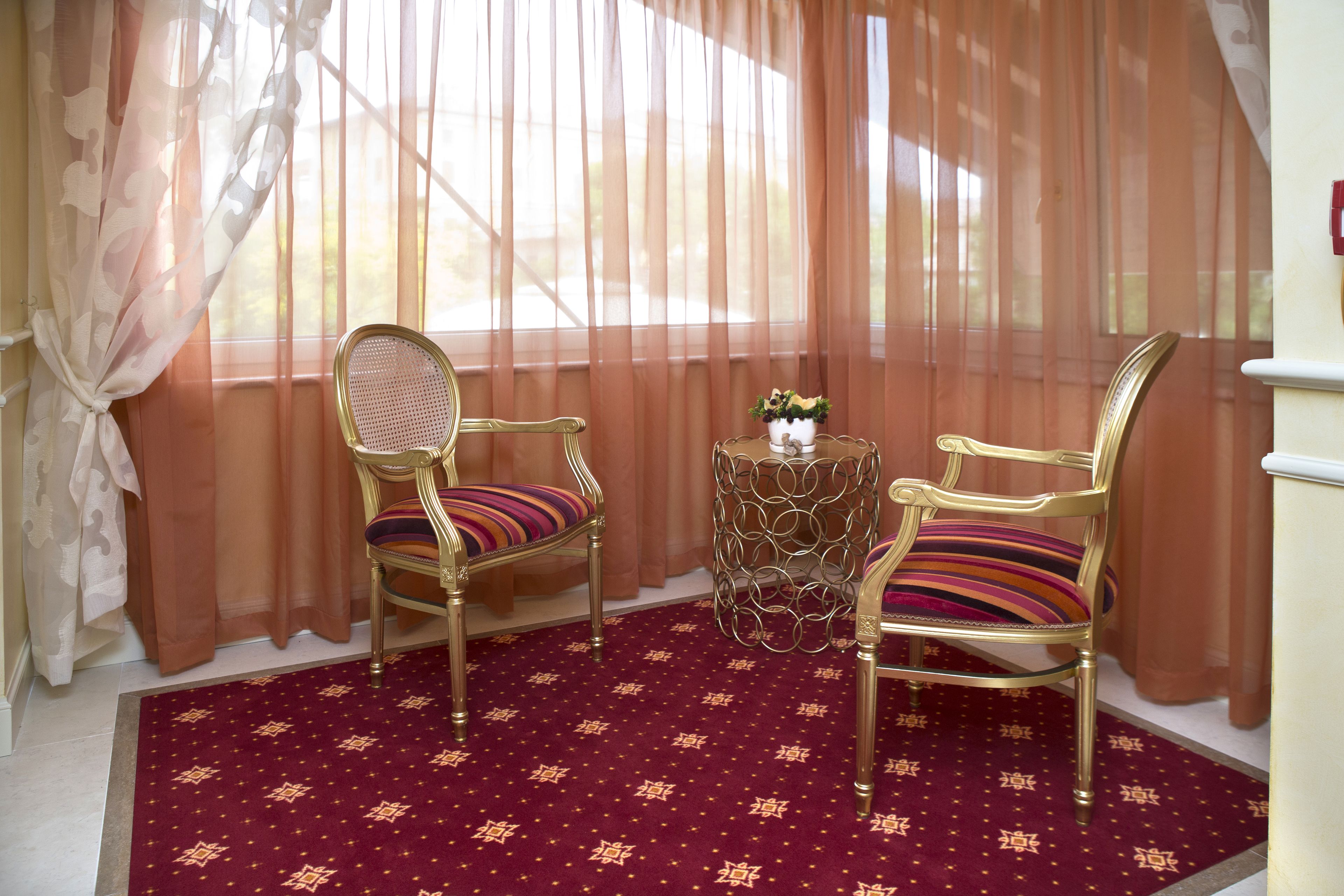 Ein Zimmer mit zwei verzierten Stühlen, einem kleinen Tisch mit einer Dekoration und einem gemusterten Teppich.