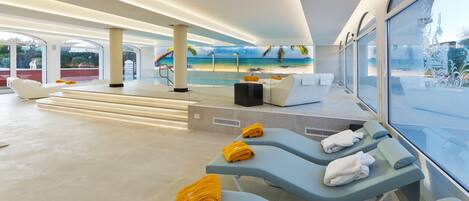 Un área de spa moderna con sillones reclinables, una piscina y vistas a la playa.