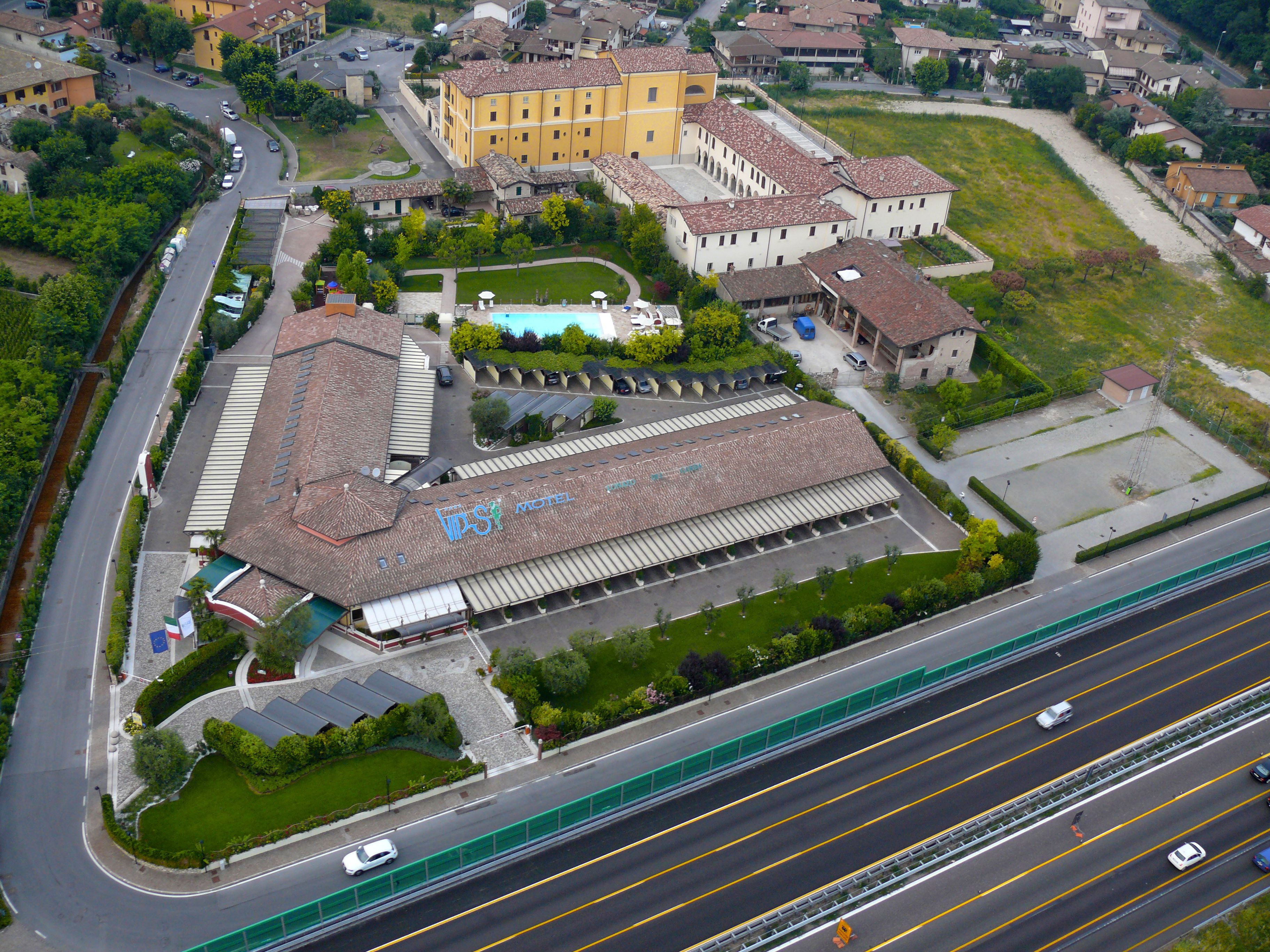 Vista aérea de un hotel con un amplio estacionamiento, piscina y un área de césped.