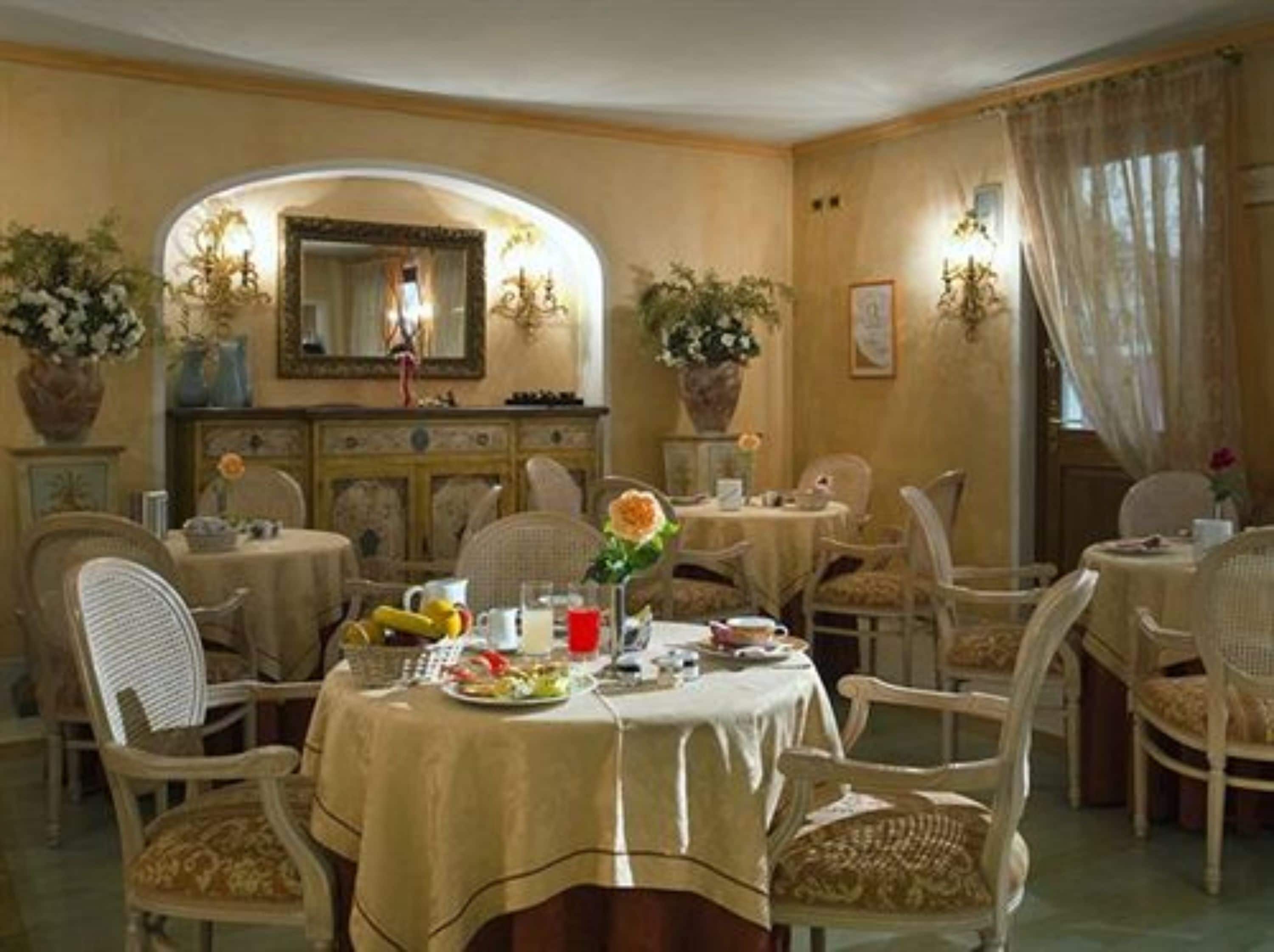 Un comedor con varias mesas redondas cubiertas con manteles color beige, rodeado de sillas de mimbre.
