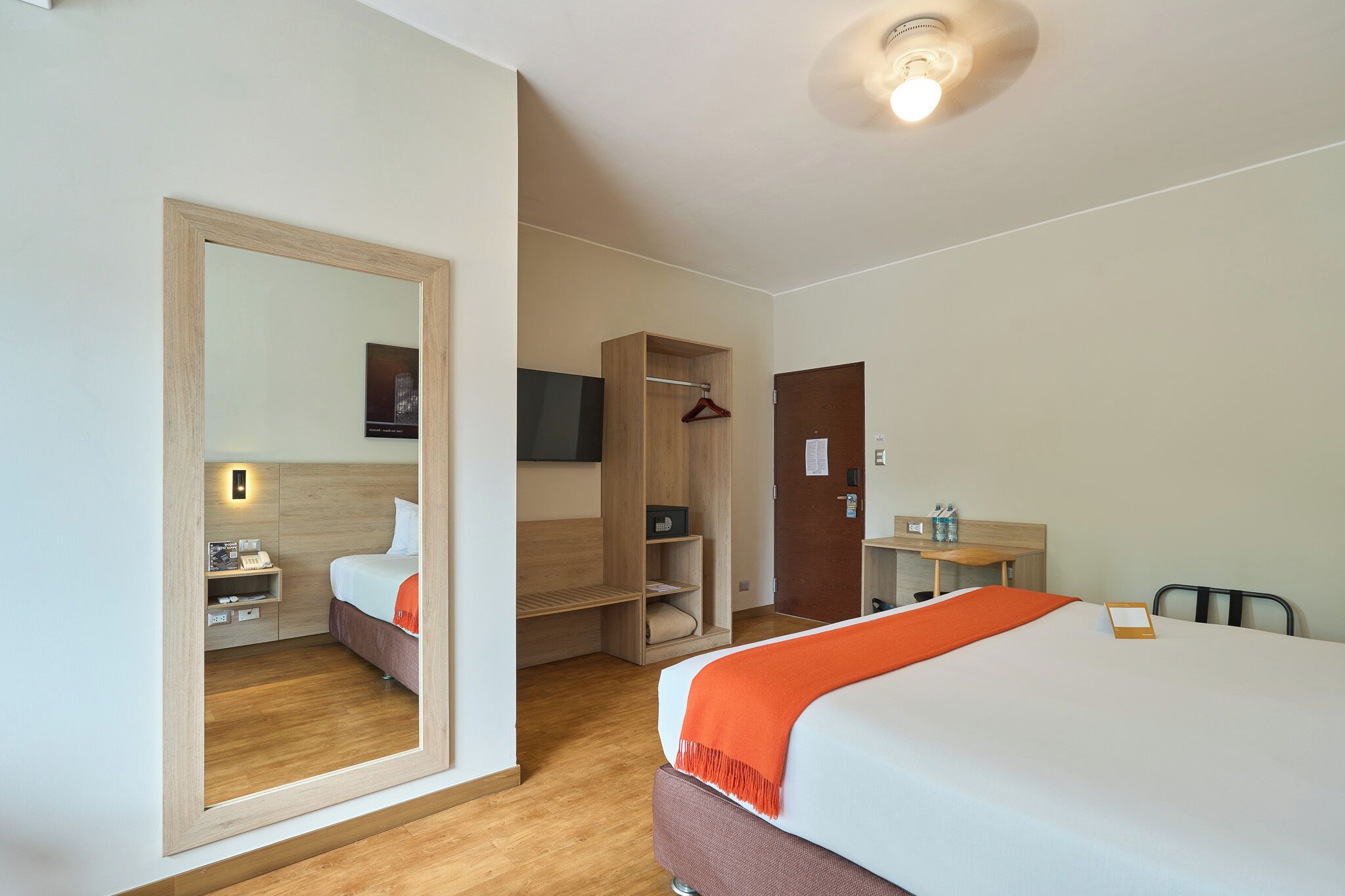 A hotel room with a bed, a wardrobe, a desk, a mirror, and a television.