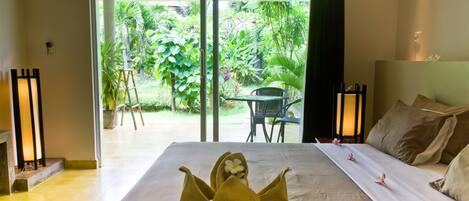 Una habitación de hotel con una cama, vistas al jardín y una mesa con sillas afuera.