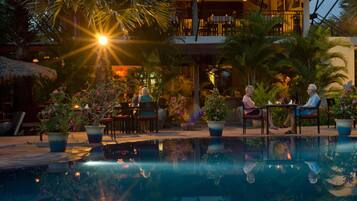 Zona de piscina con reflejo del sol, plantas en macetas y mobiliario exterior.