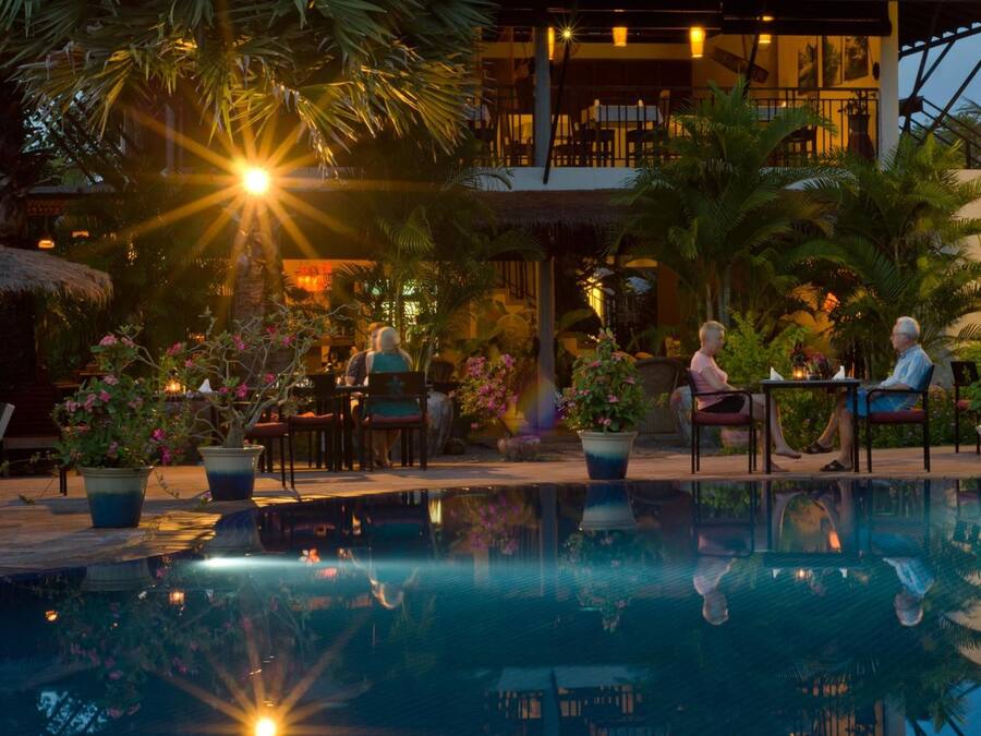 Zona de piscina con reflejo del sol, plantas en macetas y mobiliario exterior.