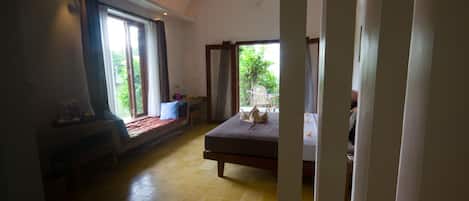 A bedroom with a bed, a window with curtains, a chair, and a small table.
