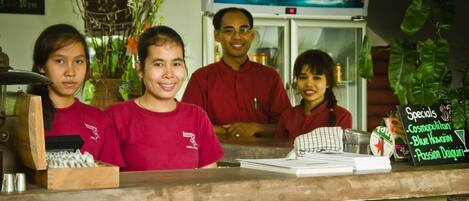 A restaurant counter with a menu board displaying specials, a refrigerator, and a television screen in the background.