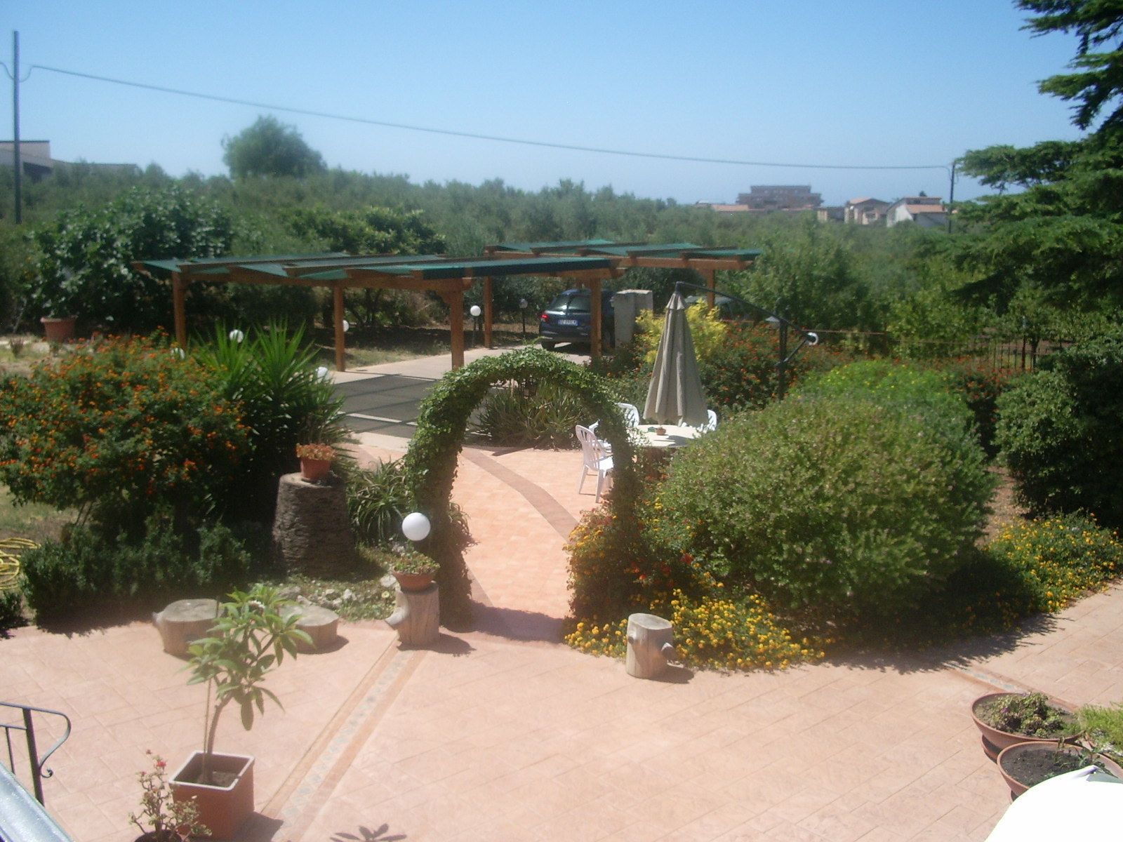 Un jardín con pérgola, mobiliario y plantas en macetas.