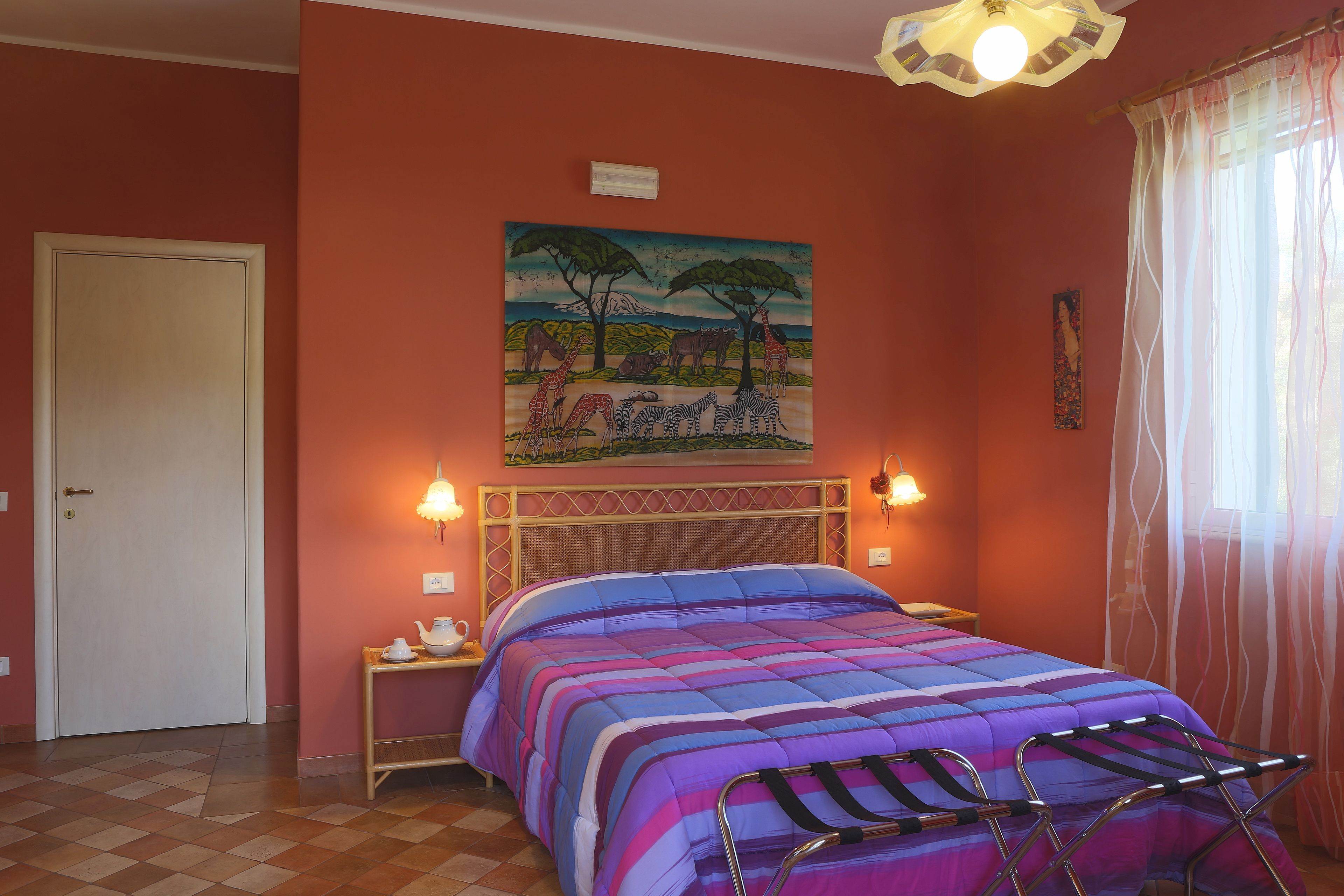 A bedroom with a bed, a painting of animals, a nightstand, and a window with curtains.