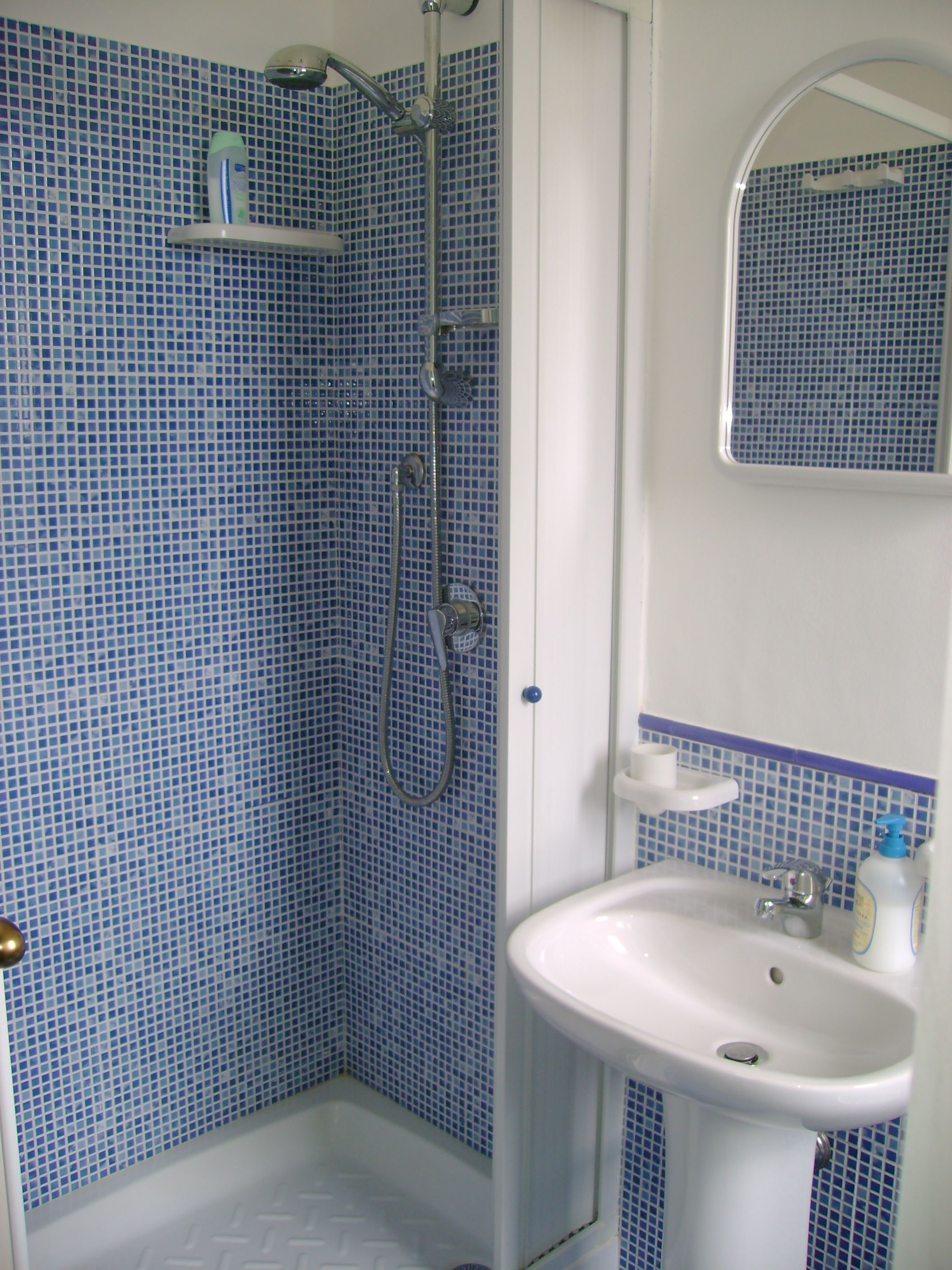 Une salle de bain avec des carreaux de mosaïque bleus, une douche, un lavabo et un miroir.