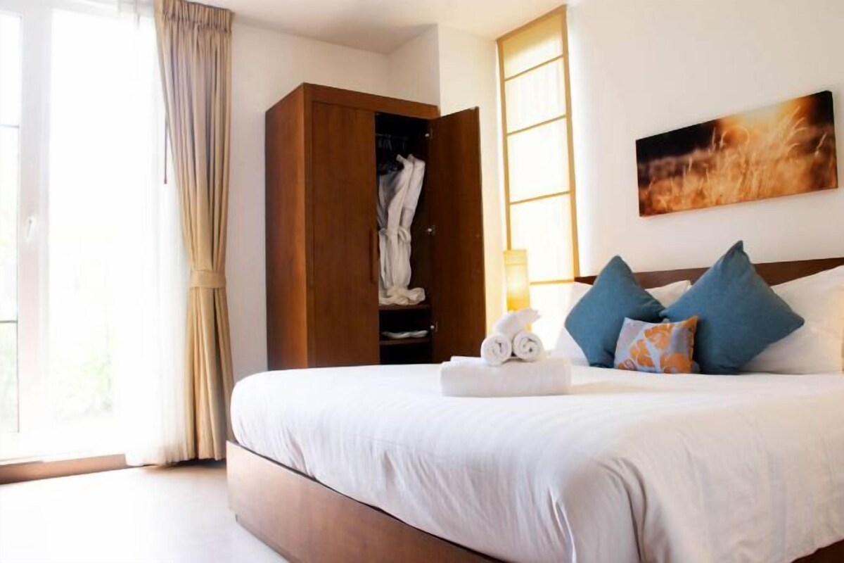 Une chambre d’hôtel avec un grand lit, une armoire, un tableau au mur et une fenêtre avec des rideaux.