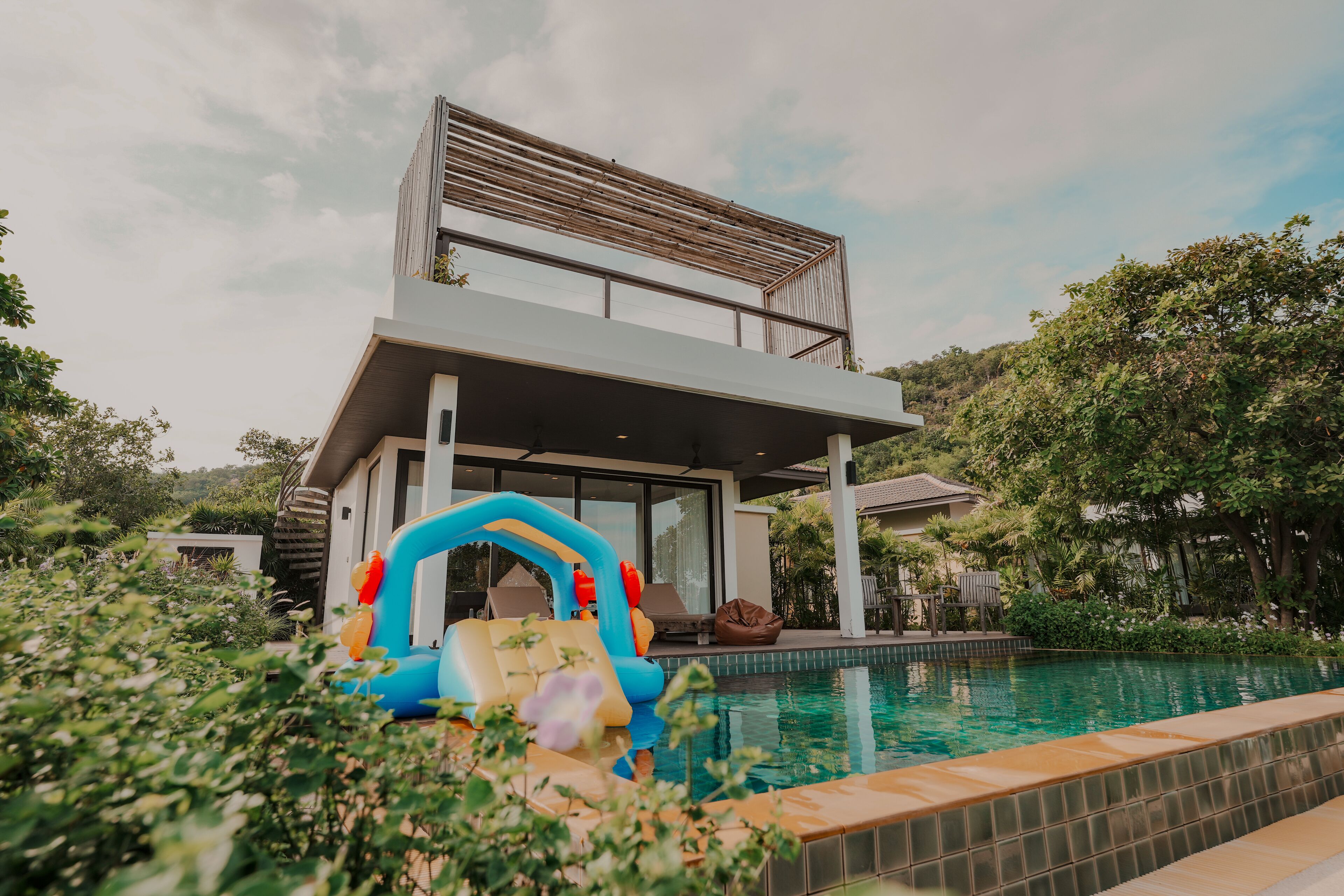A modern two-story house with a pool, surrounded by lush greenery.