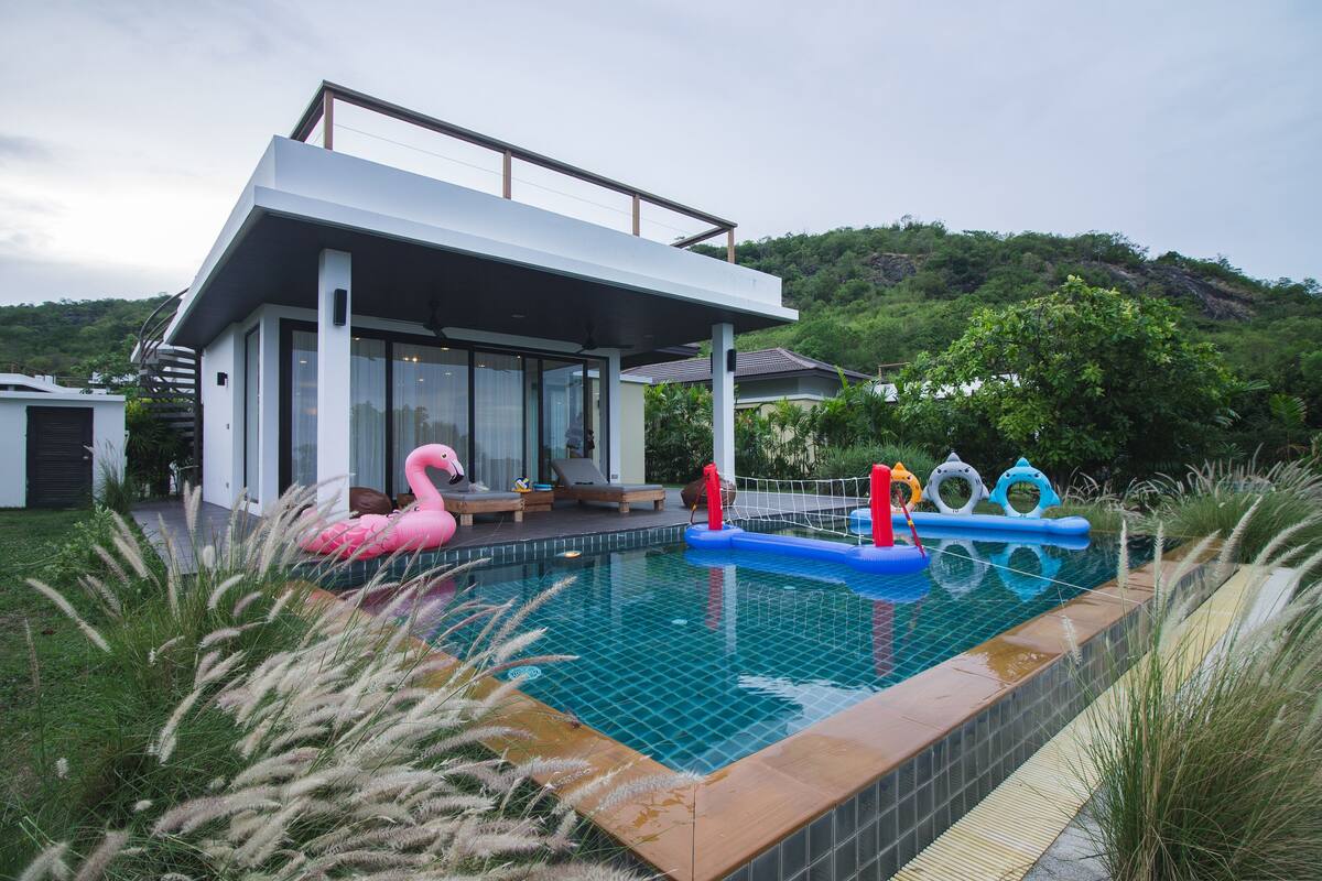 Una casa moderna con piscina, rodeada de vegetación y colinas.