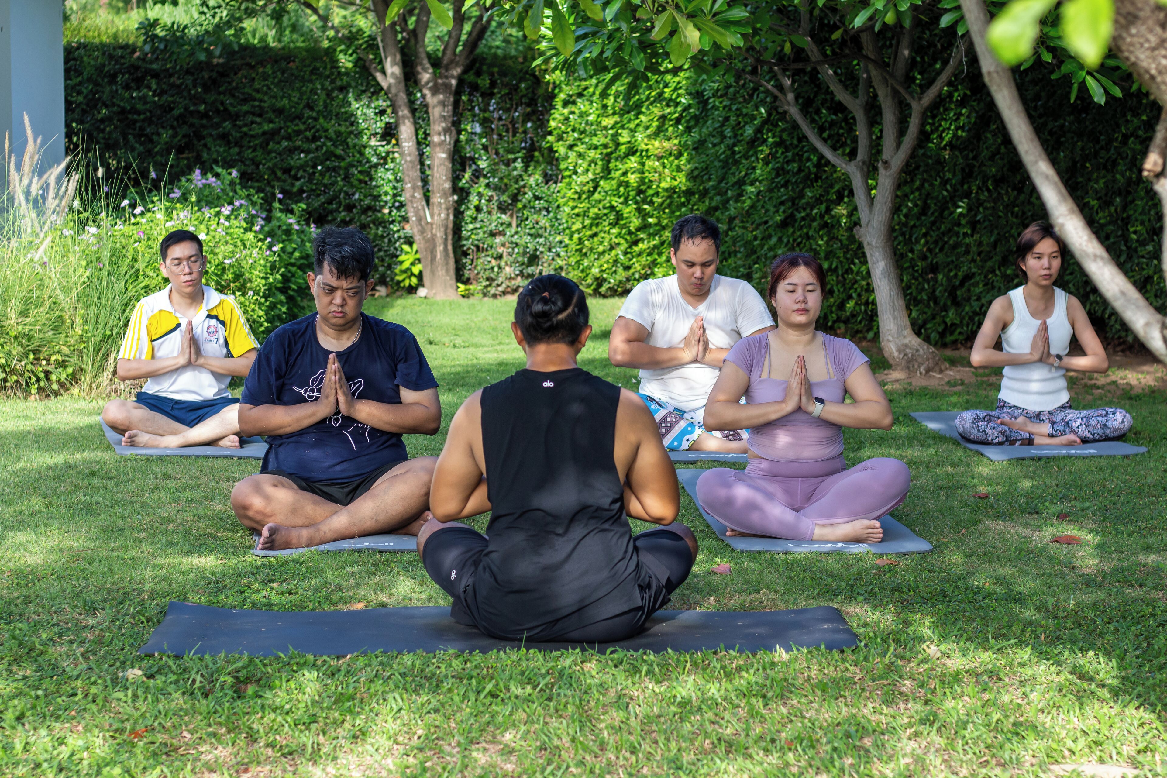 Un groupe de personnes assises sur des tapis de yoga à l’extérieur, pratiquant la méditation.