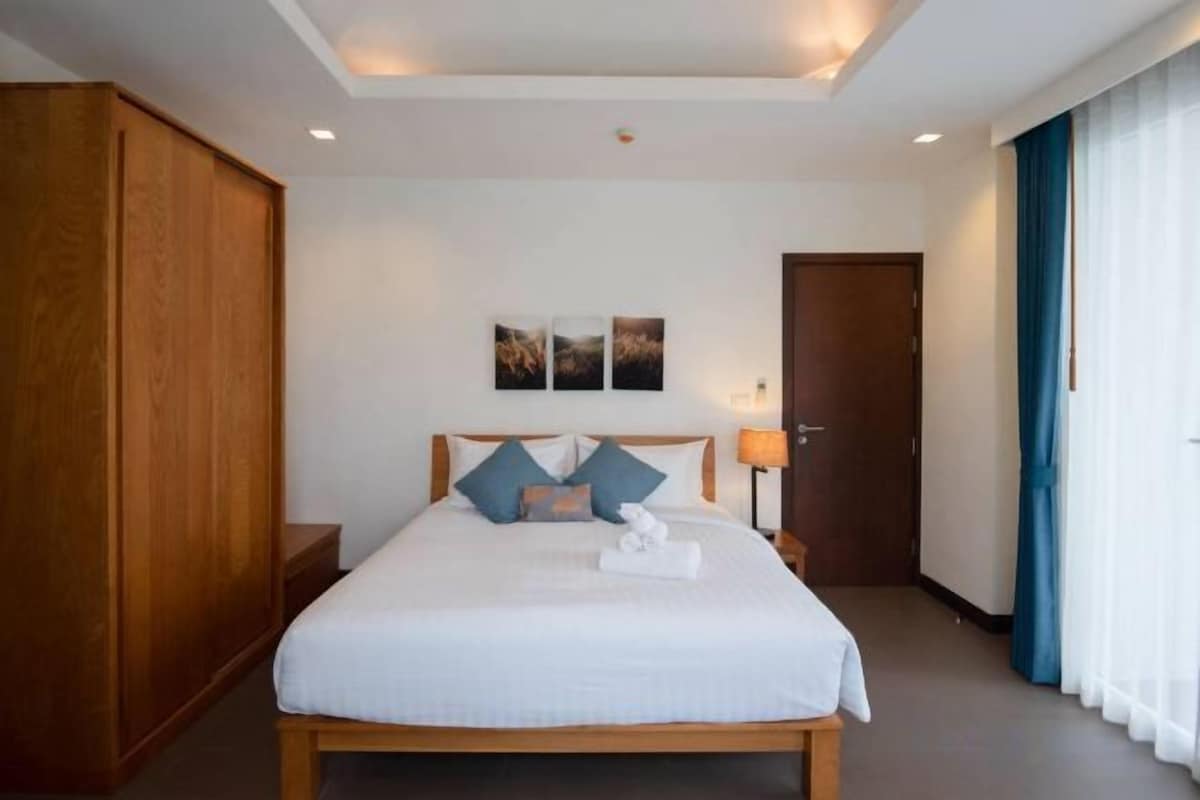 Habitación de hotel con una cama grande, un armario, una mesita de noche y una lámpara.